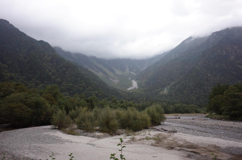 A sandy riverbed with a foggy mountain valley in the background