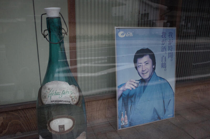 A storefront window with a huge bottle and an old poster